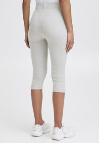 Leggings capri gris à côtes avec un design ajusté, taille mi-haute et longueur courte, accompagnés de baskets sportives blanches.