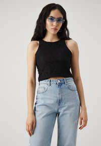 Fekete csipkés crop top, ujjatlan kivitelben, világoskék, magas derekú, koptatott farmernadrággal párosítva. Szív alakú fülbevalókkal kiegészítve.