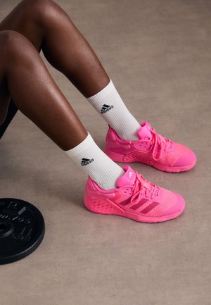 Zapatillas deportivas rosa brillante que cuentan con materiales de malla y sintéticos, acentos texturizados y calcetines blancos con detalle de logotipo negro.