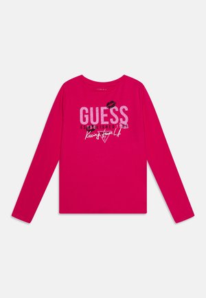 Lyserød langærmet skjorte med teksten "GUESS Established 1981 Kissing from L.A." og et sort læbestifttryk over logoet.