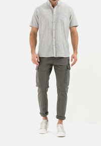 Hellgrau kurzärmliges Hemd mit Brusttasche und Holzknöpfen, kombiniert mit dunkelgrauen Cargo-Hosen mit Seitentaschen und weißen Sneakers.