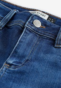Tumši zili denim šorti ar vidēju jostas augstumu, kas apvieno metāla pogas aizdari, oranžs šuvums un etiķete ar izmēru EU 36.