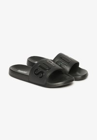 Sorte slip-on sandaler med en bred rem, der har forhøjet "SUPERDRY" tekst. Glat syntetisk materiale, flad sål og minimalistisk design.