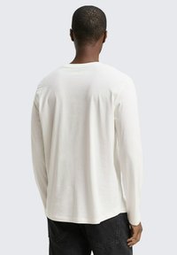 Witte katoenen blouse met lange mouwen en een ronde halslijn, met een gladde textuur en een ontspannen pasvorm, gedragen met donkere spijkerbroek.