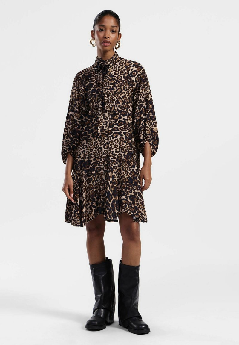 Abito con stampa leopardata nei toni del marrone e nero; presenta un colletto alto, maniche a sbuffo e un orlo svasato. Abbinato a stivali neri al ginocchio.