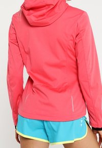 Fitted pink lightweight jacket with a hood, visible seams, and reflective accents. Paired with bright blue shorts with yellow trim.