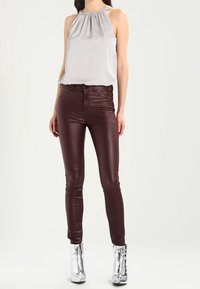 Grå halterneck-top med rynkad halslinje, kombinerad med burgundyröda fusk-läderbyxor och metalliska silverfärgade ankelskor. Enfärgad bakgrund.