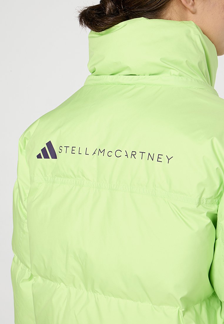 Donna che indossa un giaccone imbottito verde chiaro con il logo di Stella McCartney e il simbolo Adidas sulla parte superiore della schiena.