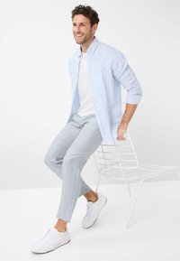 Light blue striped shirt over a white t-shirt, paired with light gray pants and white sneakers. Sitting on a minimalist white metal chair.
