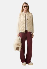 Pikowana, kremowa kurtka ocieplana z szarymi rękawami i logo; bordowe spodnie; beżowe buty na platformie; trzyma torebkę z futra syntetycznego.