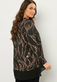 Schwarze Bluse aus fließendem Stoff mit einem abstrakten Blattmuster in Rosa und Beige. Lange Ärmel und ein leicht längerer Saum hinten.