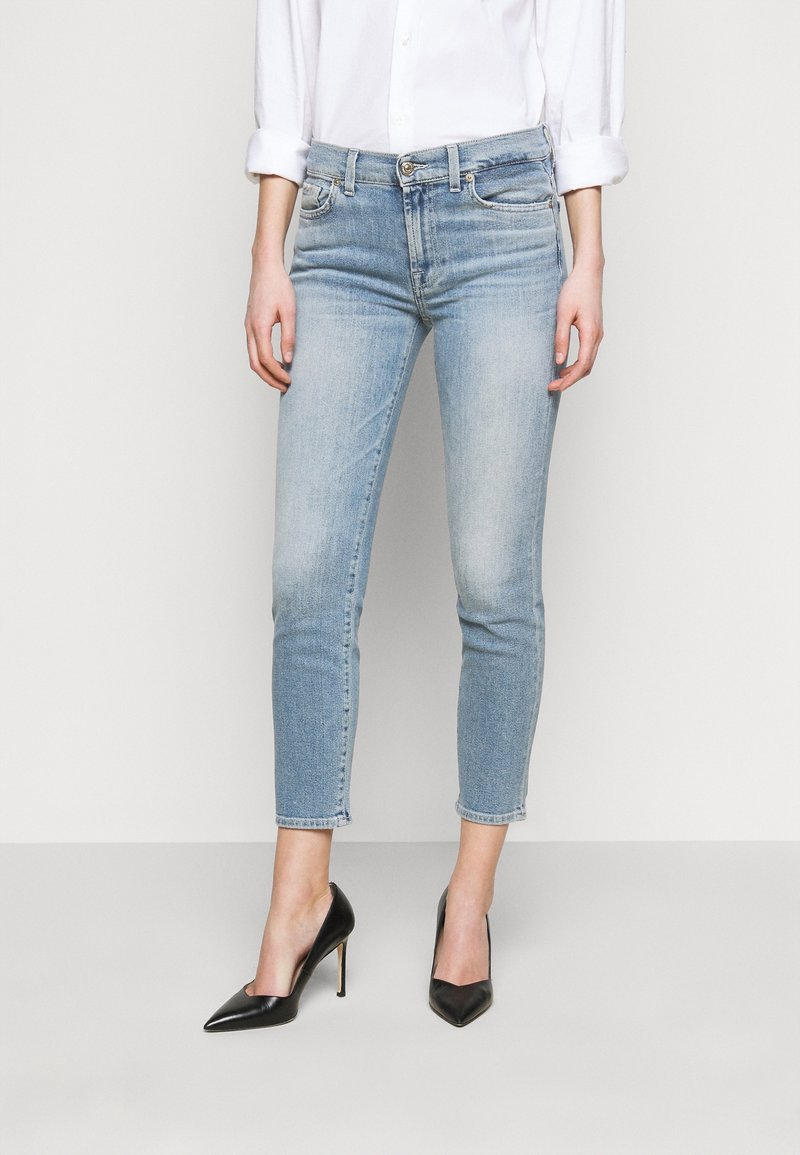 Jeans de mezclilla azul claro con un corte ajustado, de longitud recortada y un ligero desgastado. Combinados con tacones altos negros de punta y una camisa blanca.