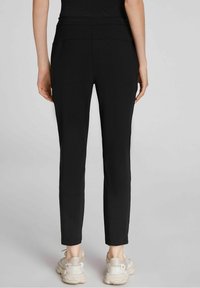 Pantalones ajustados negros con una textura suave, cintura de media altura y piernas entalladas, combinados con zapatillas deportivas de color claro.