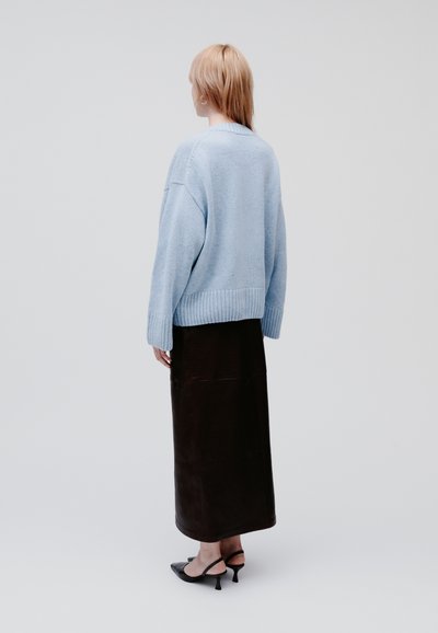 Light blue knit sweater with ribbed hem, paired with a long brown leather skirt and black slingback heels, viewed from the back.