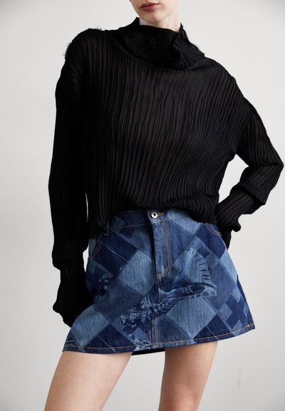 Črna nabrana bluza z dolgimi rokavi v kombinaciji z modrim denim mini krilom s strukturiranim diamantnim vzorcem in natisnjenim dizajnom. Poudarjena s sprednjim gumbom.