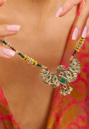 Goldkette mit Smaragd- und roten Akzenten, ausgestattet mit einem detaillierten Adleranhänger und einer mehrfarbigen Perlenkette, die lebendige Texturen zeigt.