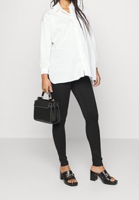 Camisa blanca de botones, vaqueros ajustados negros, mules negros de tacón con hebilla y un bolso negro con detalles dorados. Texturas suaves, diseño casual.