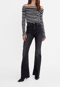 Zwart-wit gestreepte off-shoulder top met lange mouwen, gecombineerd met hoge zwarte flared jeans met openingen aan de zoom.