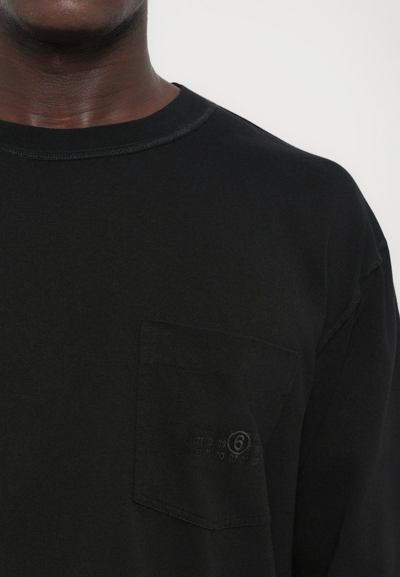 Chemise noire à manches longues en coton, dotée d'un col rond, de coutures texturées et d'une poche sur la poitrine gauche avec un motif embossé.