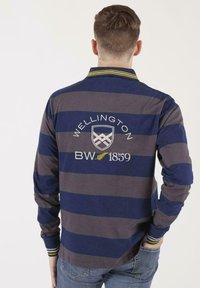 T-shirt de rugby à manches longues avec des rayures horizontales bleu marine et gris, logo brodé "Wellington BW 1859" et accents de col rayés.