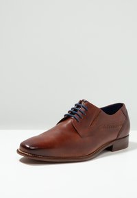 Chaussure habillée en cuir marron avec une finition lisse, bout pointu, lacets bleus et couture décorative sur le côté. Talon bas empilé.