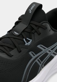 Čierna športová obuv s textúrovaným vrškom, časťami z mriežky, sivými prvkami a odolnou gumovou podrážkou s výrazným logom.