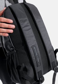 Zaino nero con tessuto testurizzato, sezioni imbottite, spallacci regolabili e una tasca laterale. Presenta un'etichetta "PLANET WATER".