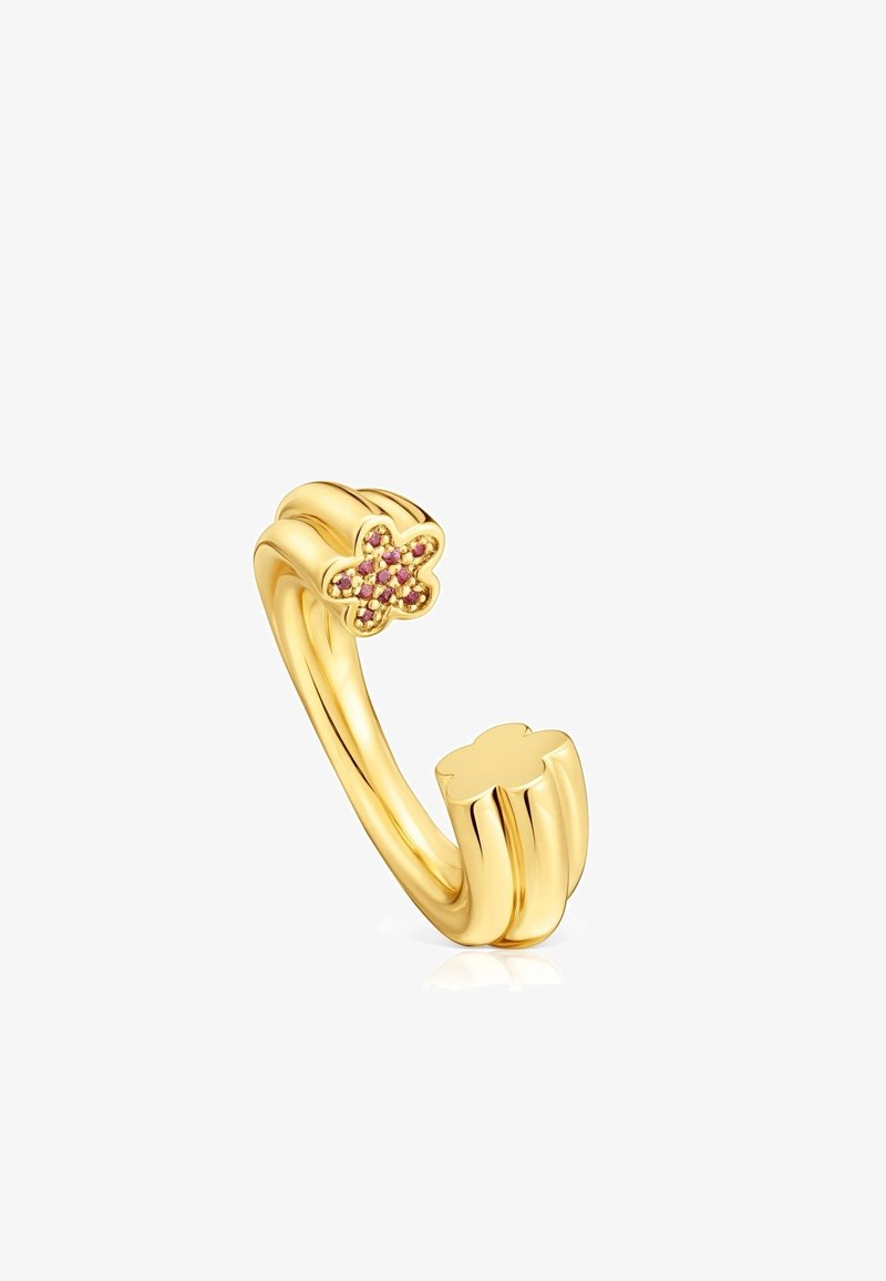 Bague en métal doré avec un design de bande torsadée, ornée d'une petite fleur avec des pierres précieuses roses et jaunes. Texture lisse avec une finition polie.