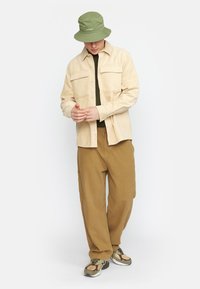Beige corduroy overhemd met borstzakken, olijfgroen muts, bruine cargobroek en multicolor sneakers. Casual, losse pasvorm.