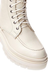 Bottines en cuir blanc avec une finition texturée, un laçage sur le devant et une semelle en caoutchouc chunky et crantée pour une meilleure adhérence.