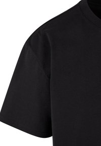 T-shirt noir en coton à manches courtes montrant l'épaule et la manche gauche supérieures avec un col rond.