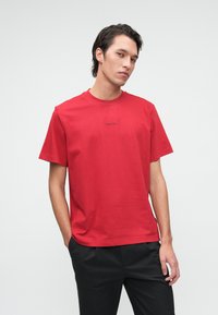 Czerwona bawełniana koszulka z okrągłym dekoltem, krótkimi rękawami i małym czarnym logo na piersi. Połączona z czarnymi spodniami.