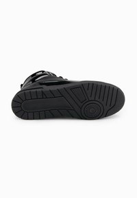 Černá podrážka tenisky s texturovaným gumovým dnem a kulatým vzorem dezénu, který zajišťuje přilnavost a odolnost.