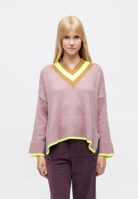 Világos rózsaszín, nagy méretű pulóver mély V-nyakkivágással, sárga és barna kötött díszítésekkel a nyakrésznél és az alján. Texturált anyag.