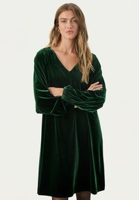 Grünes Samtkleid mit V-Ausschnitt, langen Puffärmeln und A-Linien-Silhouette, das eine weiche Textur und ein luxuriöses Erscheinungsbild aufweist.