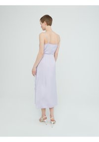 Licht lavendel midi-jurk met dunne bandjes, gladde stof en een aansluitende taille. Heeft een zijslit en valt soepel tot aan de enkels.