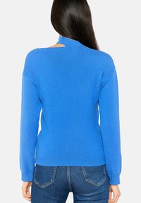 Pull bleu à manches longues avec un détail découpé au dos. Fabriqué en tissu tricoté texturé. Présente une coupe décontractée et un ourlet côtelé.