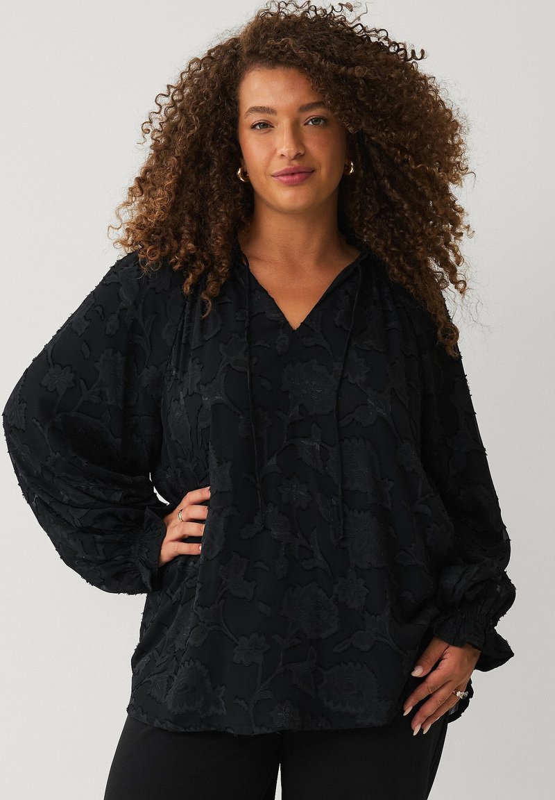 Sort hoodie med blomsterprint, V-hals, snørelukning og voluminøse ærmer. Fremstillet af blødt stof med en tekstureret overflade.