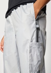 Šviesiai pilkos kelnės su kišenėmis, pagamintos iš lygaus audinio, su šonine kišene ir etikete ant juosmens, laisvo silueto.