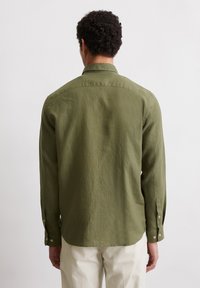 Long-sleeve shirt in olive green fabric, featuring a straight hem, buttoned cuffs, and a spread collar. Subtle texture visible.