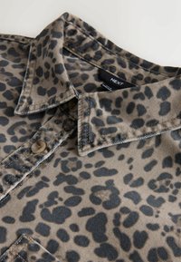 Košeľa s leopardím vzorom v béžovej a čiernej farbe, vyrobená z látky s hladkým povrchom. Má špicatý golier a dve okrúhle gombíky.