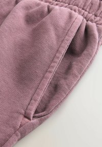 Pantalones de algodón de color rosa claro con una cinturilla elástica y bolsillos laterales. La tela tiene una textura suave y un patrón de punto sutil y uniforme.