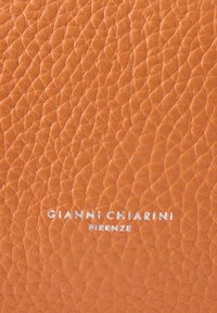 Oranžist nahast materjal tekstuurse pinnaga. Alumises osas on reljeefne hõbedane tekst "GIANNI CHIARINI FIRENZE".