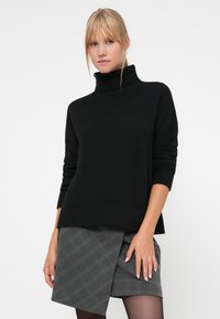Czarny, dzianinowy sweter typu turtleneck z długimi rękawami, luźny krój i ściągacz na dole, zestawiony z szarym spódnicą w kratę zapinaną na węzeł.