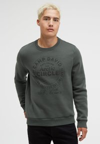 Dark green sweatshirt with a round neck, ribbed cuffs, and a front graphic featuring "Camp David" and "Arctic Circle" in black print.