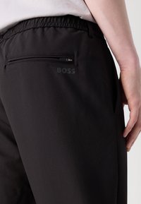Pantalons de sport noirs avec une taille élastique, dotés d'une poche arrière zippée et d'un logo "BOSS" subtilement en relief. Texture lisse.