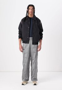 Sort vindjakke med trykknapper, parret med lysegrå puffede bukser med vandrette syninger og elastisk talje. Beige sneakers.