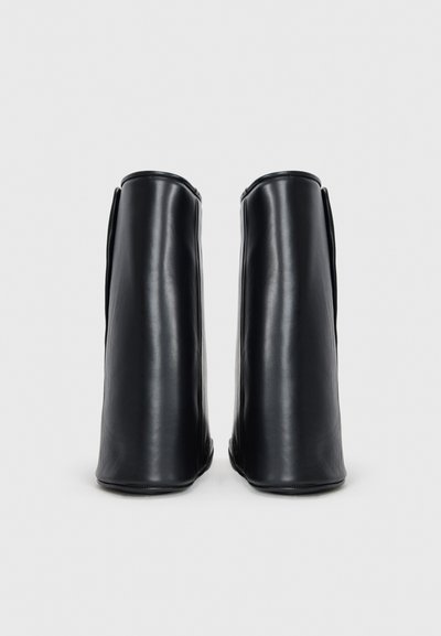 Bottines en cuir noir avec un design épuré, des têtes arrondies et une texture lisse, présentant des coutures minimales et sans matériel visible.