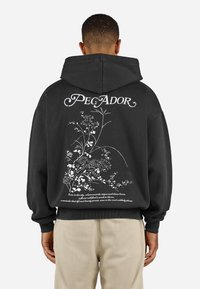 Sort oversized hoodie med et hvidt blomsterdesign og tekst på ryggen. Blødt, struktureret stof med en hætte med snor og ribbede manchetter.