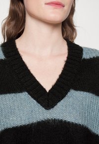 V-neck pullover featuring wide black and light blue stripes, knitted texture, and a soft, fuzzy finish.